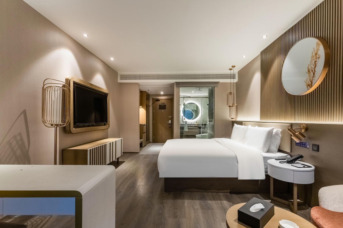A hotel room with a bed, bedside table, TV, and a mirror.