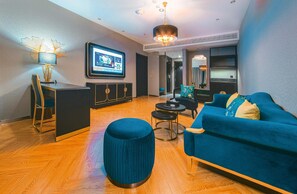Una sala moderna con un sofá azul, un otoman redondo, una mesa de centro negra y un televisor montado en la pared.