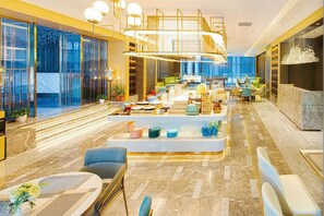 A hotel lobby with a reception desk, seating area, and a staircase leading to an upper level.