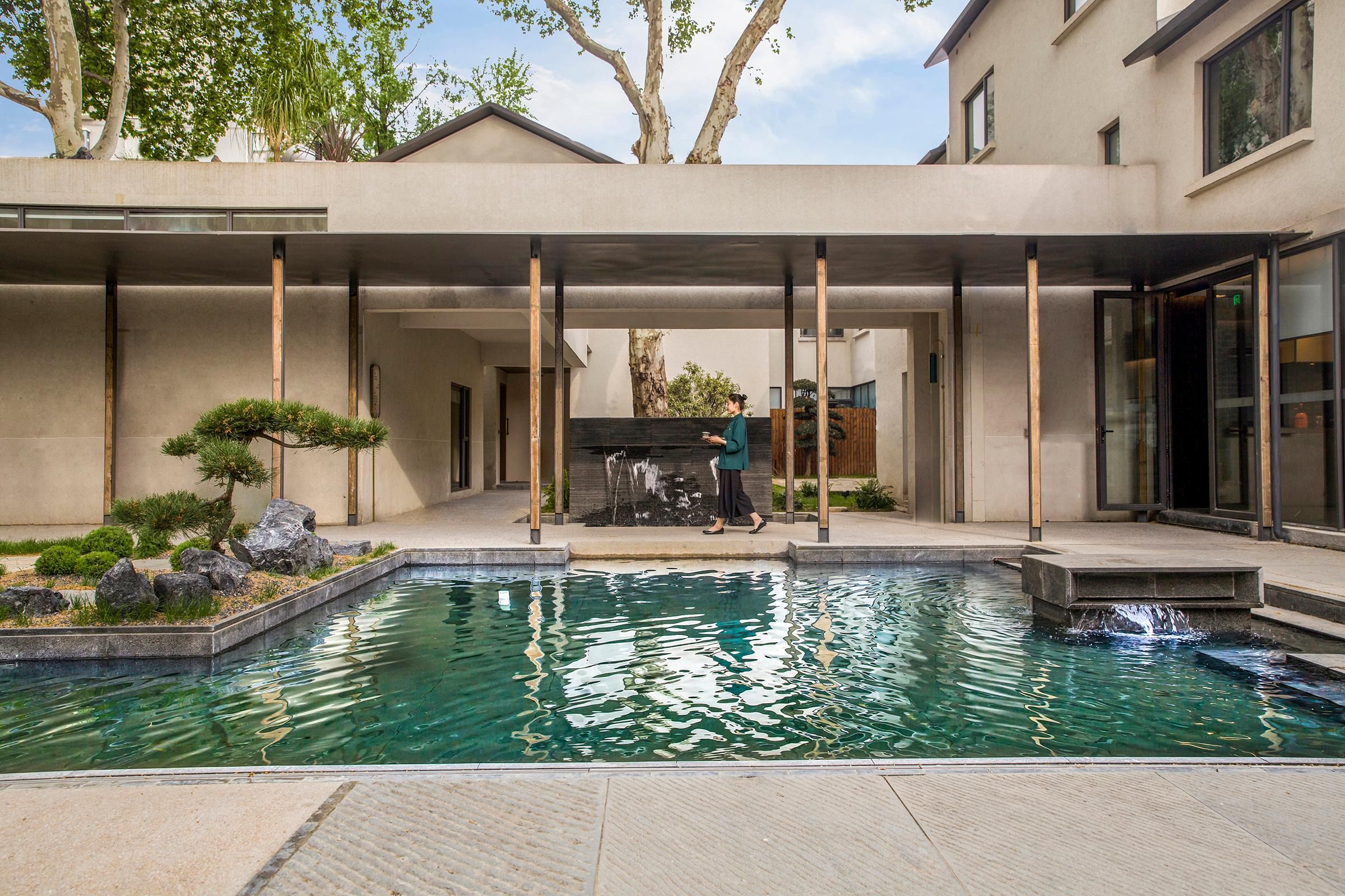 A modern pool area with a waterfall feature, surrounded by a minimalist architectural design and a small garden.