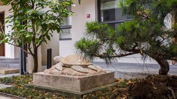 A landscaped area with a pine tree, a stone sculpture, and a building in the background.