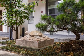A landscaped area with a pine tree, a stone sculpture, and a building in the background. - Blossom Hill Hotel Nanjing Laomendong Zhuqueli (Nanjing)