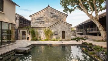A stone building with a pool in front, surrounded by greenery and trees.
