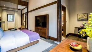 Una habitación de hotel con cama, televisión, aparador de madera y una mesa de comedor con frutero.