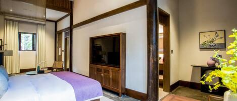 A hotel room with a bed, a television, a wooden cabinet, and a dining table with a fruit bowl.