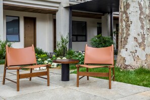 Duas poltronas de couro com estrutura metálica e uma pequena mesa redonda em um pátio, com um edifício ao fundo.