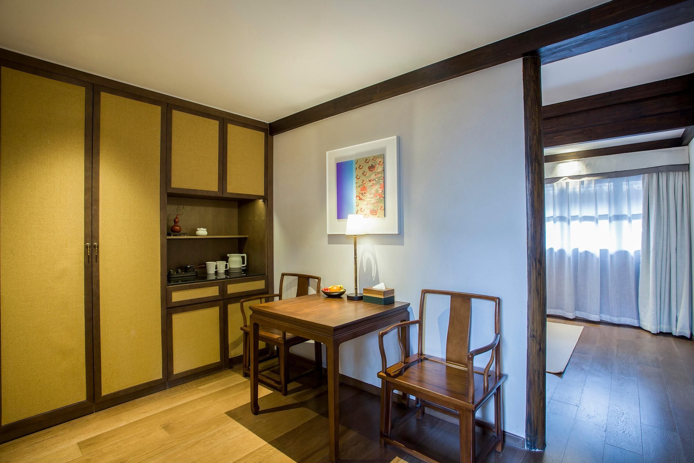 A dining area with a wooden table and chairs, a small shelf with kitchen items, and a framed picture on the wall.