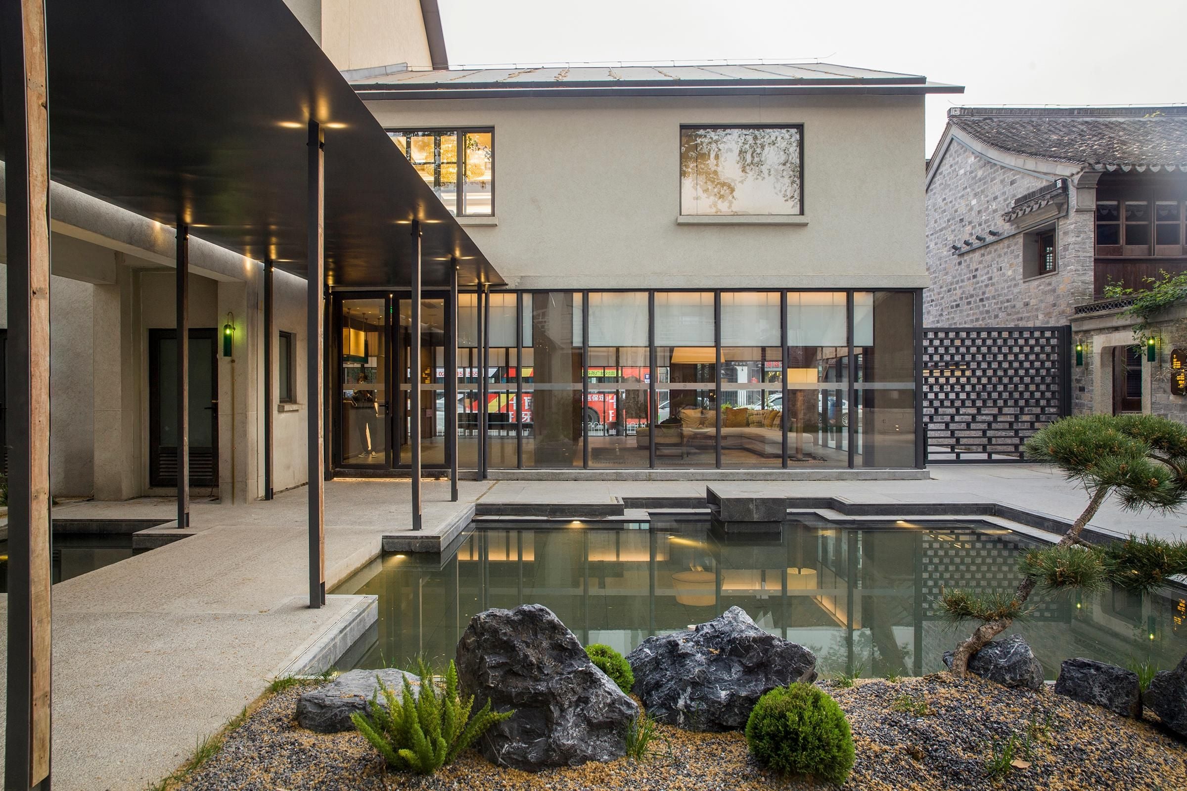 A modern building with a glass facade, a courtyard with a reflective pool, and traditional architecture on one side.