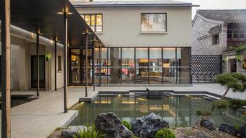 A modern building with a glass facade, a courtyard with a reflective pool, and traditional architecture on one side.