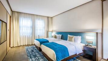 A hotel room with two beds, a nightstand, a lamp, and a large window with curtains.