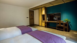 Habitación de hotel con dos camas, un escritorio con silla, televisión y una mesita con una planta.