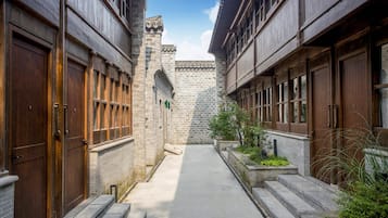 Un carrer estret entre dos edificis amb portes i finestres de fusta, una paret de pedra i un cel serè.