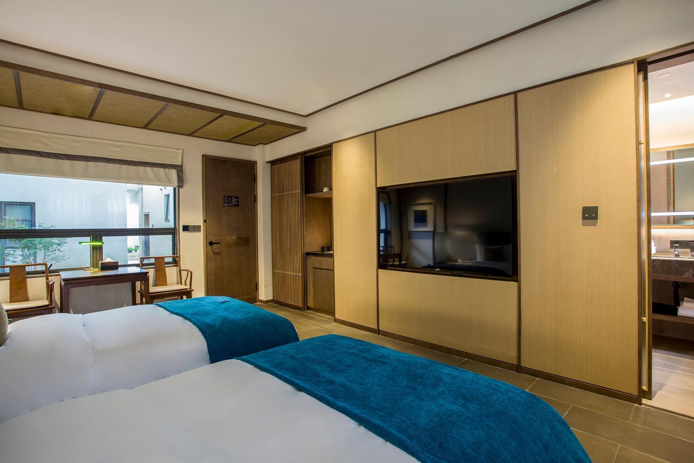 A hotel room with two beds, a TV, a desk, and a window with a view.