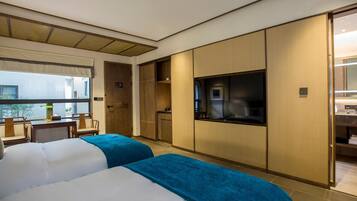 A hotel room with two beds, a TV, a desk, and a window with a view.