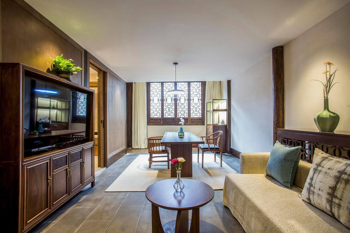 Uma sala de estar moderna com um centro de entretenimento de madeira, uma mesa de jantar com cadeiras, um sofá e um vaso decorativo.