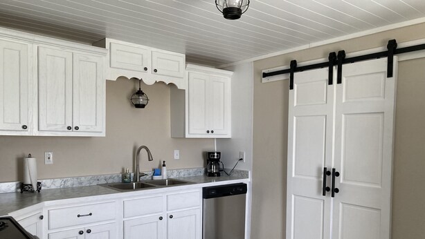A kitchen with white cabinets, a dishwasher, a coffee maker, and a sliding barn-style door. - Newly remodeled offers many amenities with perfect location! (Ironton)