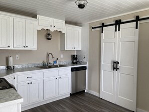 Una cocina con gabinetes blancos, lavavajillas, cafetera y puerta corredera estilo granero.