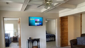 A living room with a ceiling fan, a TV mounted on the wall displaying streaming services, a bed with a patterned bedspread, and a brown leather couch. - Newly remodeled offers many amenities with perfect location! (Ironton)