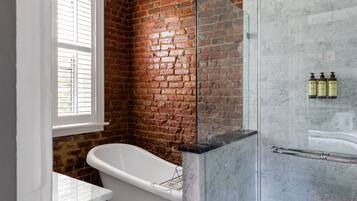 Un baño con pared de ladrillo, una bañera independiente, ducha con mampara de vidrio y suelo estampado.
