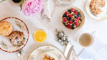 Mesa de café da manhã com diversos alimentos, uma xícara de café e um arranjo floral.