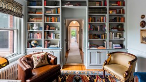 A library with bookshelves, a leather sofa, a patterned rug, and a wooden chair.