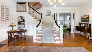 A staircase with a patterned carpet, a dining area with a table and chairs, and a chandelier.