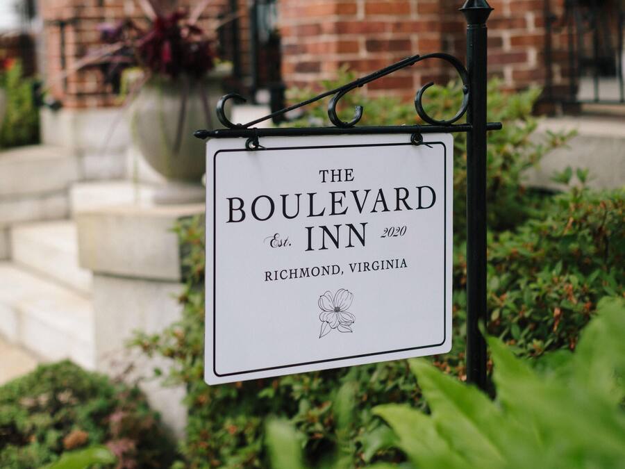 A sign for The Boulevard Inn, Richmond, Virginia, with a brick building and greenery in the background.