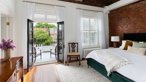 A bedroom with a large bed, a wooden chair, a small table, and a view of the outside.