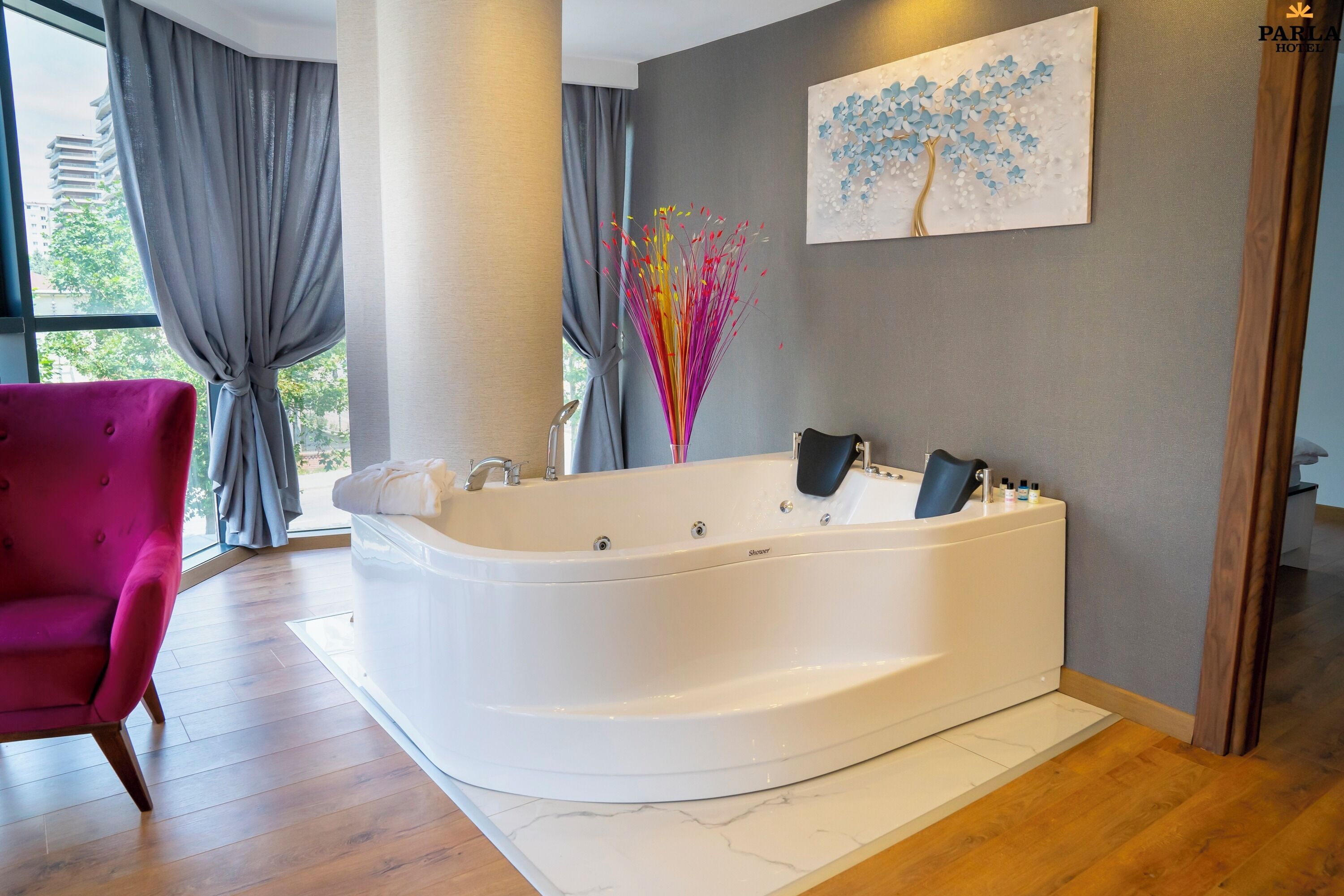 A modern bathroom with a freestanding bathtub, a pink chair, and a painting of a tree on the wall.