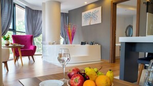 Una habitación de hotel moderna con una mesa de comedor de madera, un cuenco de fruta, una copa de vino y una silla rosa.