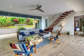 A modern living room with a sofa, coffee table, and colorful chairs. A staircase with wooden steps leads to another level. - Ocean View over Bahia Ballena's amazing Whale Tail (Uvita)