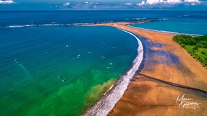 Luchtbeeld van een strand met helder turquoise water, een golvende kustlijn en boten.