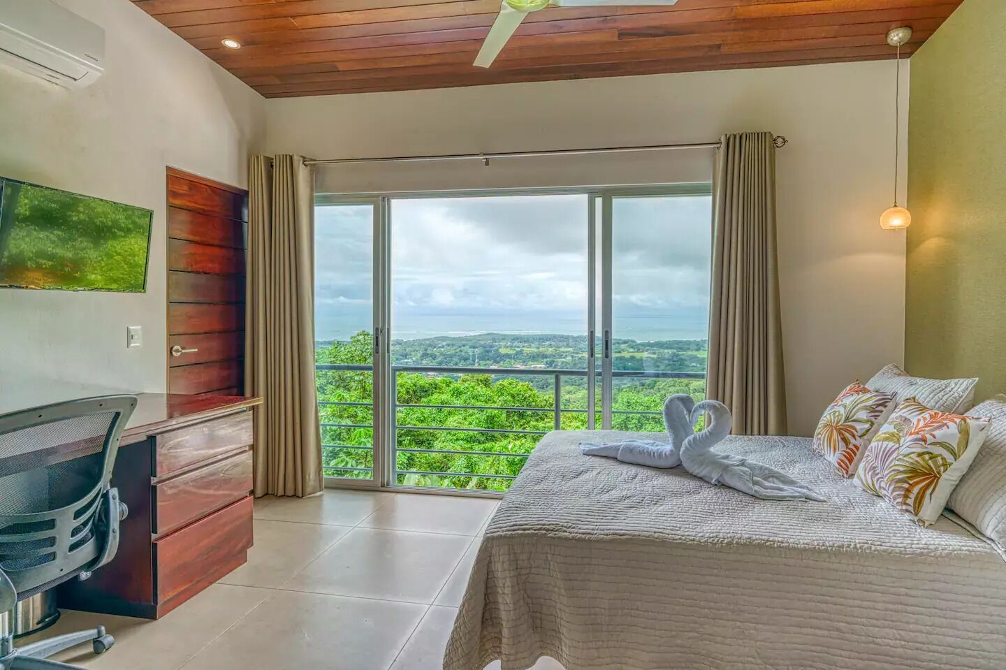 Une chambre à coucher avec un lit, un bureau et une grande fenêtre donnant sur un paysage verdoyant.