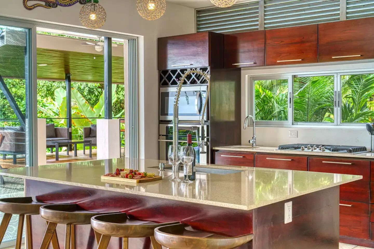 Une cuisine moderne dotée d’un grand îlot central, de tabourets de bar et offrant une vue sur une végétation luxuriante.