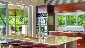 Een moderne keuken met een groot eiland, barkrukken en uitzicht op weelderige begroeiing.