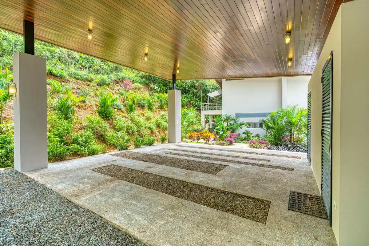 Un espacio al aire libre cubierto con piso de concreto, rodeado de abundante vegetación y una ladera.