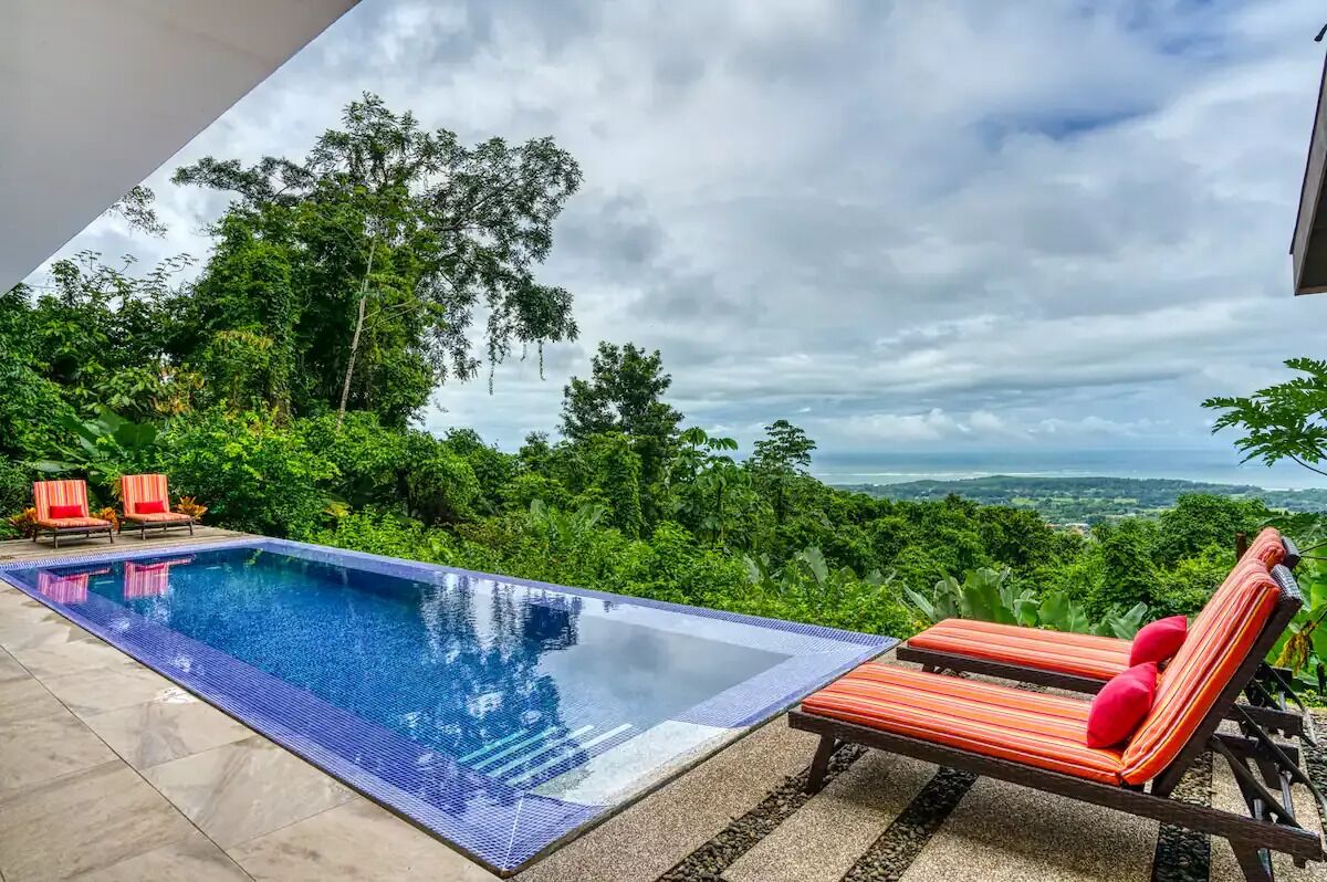 An infinity pool with lounge chairs and a view of a lush landscape.