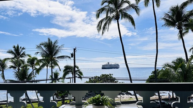 A balcony with a view of the ocean, palm trees, and a cruise ship. - OCEAN Front Kona Studio - Spectacular view! (Kailua-Kona)