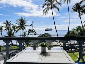 Un balcone con vista sull'oceano, palme e una nave da crociera.