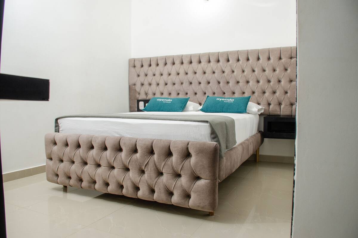 Une chambre à coucher moderne avec une tête de lit capitonnée, un lit recouvert de draps blancs et des coussins de couleur turquoise.