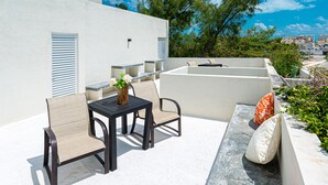 Un patio al aire libre con una mesa y sillas, un pequeño jarrón decorativo y una zona de estar con cojines.