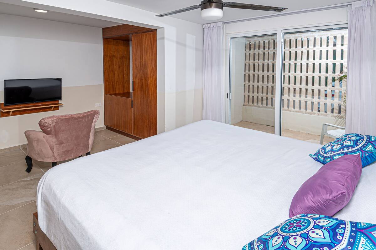 A hotel room with a bed, a TV, a chair, and a sliding glass door to the balcony.