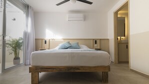 Un dormitorio moderno con estructura de cama de madera, un ventanal con cortinas, un ventilador de techo y una mesita de noche con lámpara.