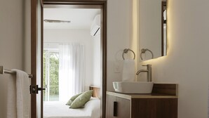 Un baño moderno con un lavamanos blanco, un inodoro y una cama visible a través de una puerta abierta.