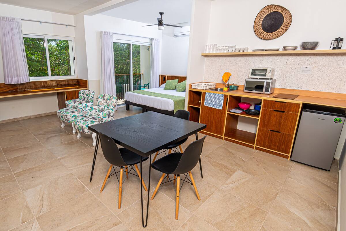 A modern kitchen with a dining area, a bed with a balcony view, and a ceiling fan.