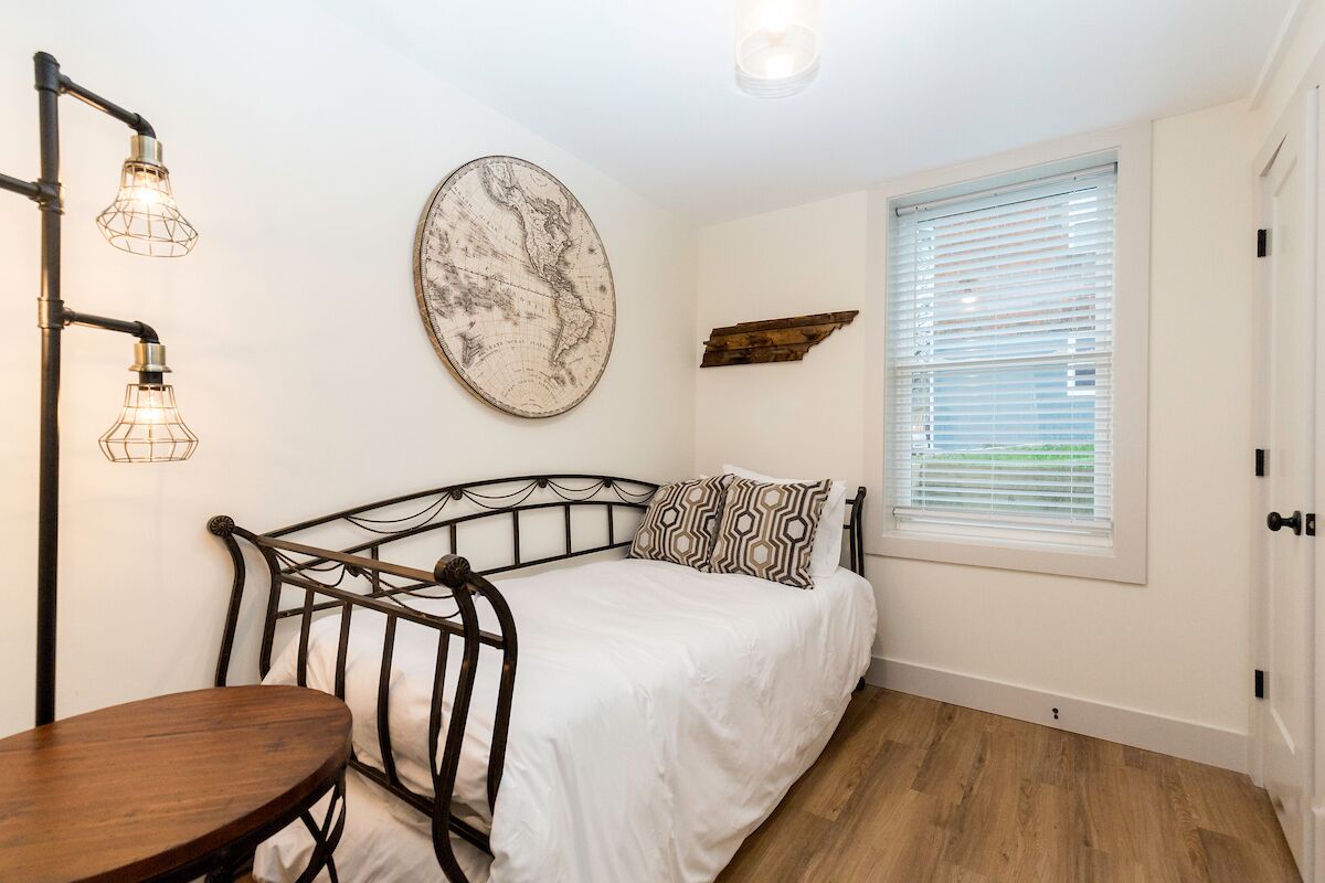 A bedroom with a metal bed frame, a round wall map, a window with blinds, and a table.