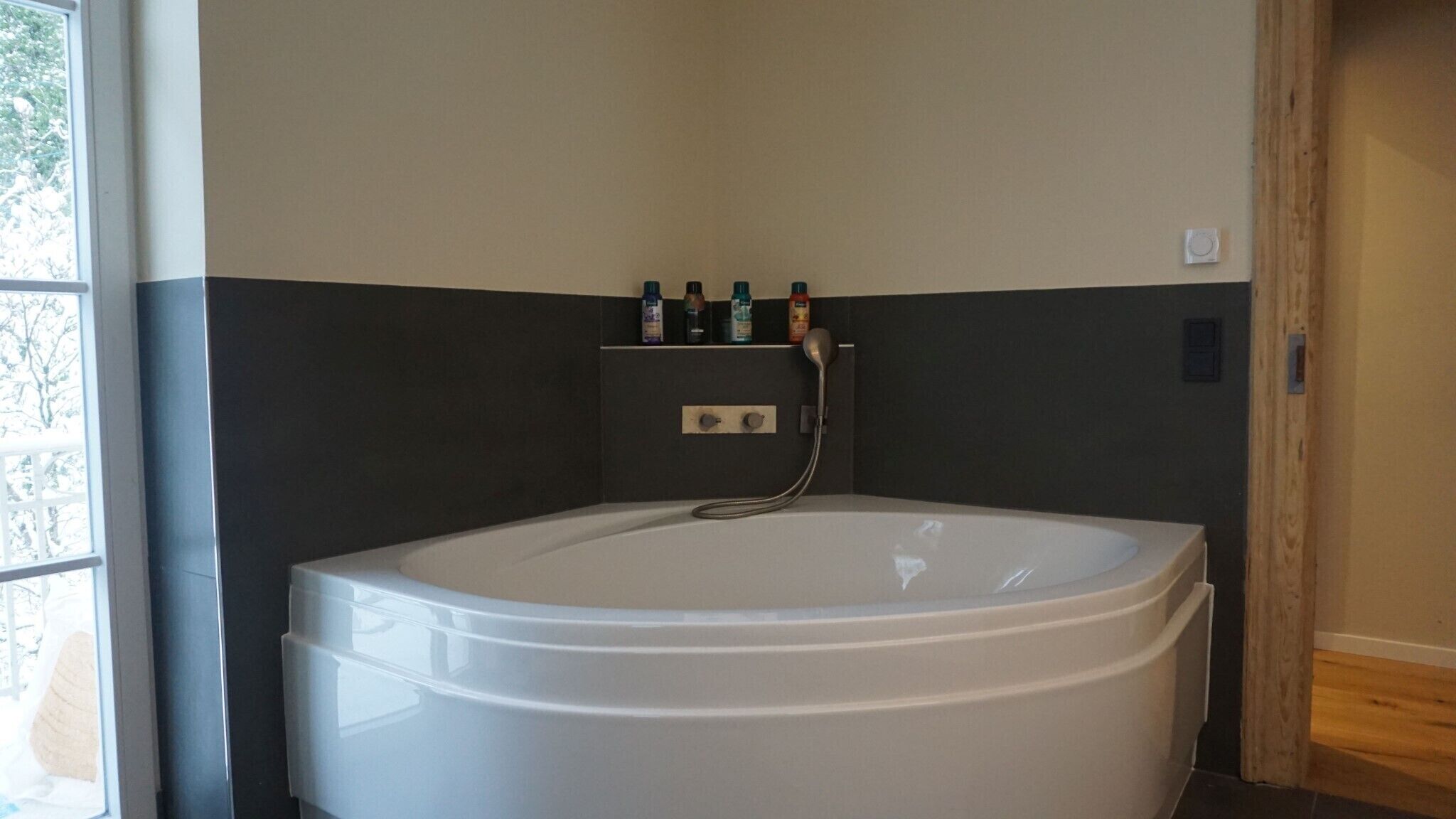 Een moderne badkamer met een groot, wit bad, een douchekop en een plank met toiletartikelen.