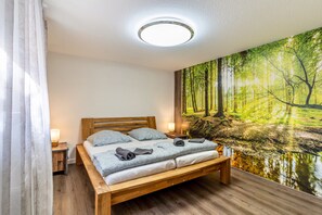 A bedroom with a wooden bed, a nightstand, a lamp, and a forest mural on the wall. - Apartment 'Ribeiro Tesouro' with Wi-Fi (Friesenheim)