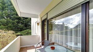 Un balcon avec une chaise, une petite table et une vue sur des arbres et un immeuble.