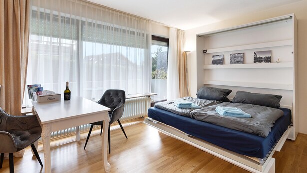 Une chambre à coucher comprenant un lit, un bureau, une chaise, un radiateur et une fenêtre avec des rideaux.